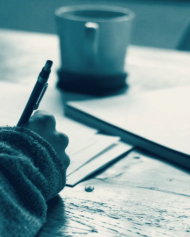 Manos escribiendo sobre unos papeles junto a un café